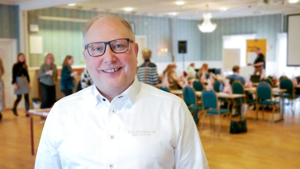 Man med glasögon och vit skjorta som ler mot kameran